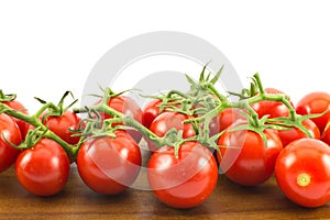 Close up of red small cherry tomatoes on a wooden surface and white background