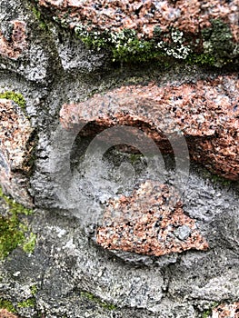 Close-up of a red stone wall with germinate moss around. Wall of sharp stones with sprouted moss