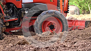 Close-up the red tractor is plowing the soil