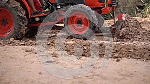 Close-up the red tractor is plowing the soil, slow motion.