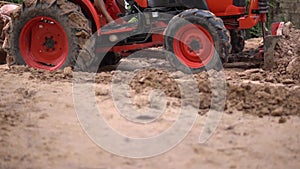 Close-up the red tractor is plowing the soil, slow motion.