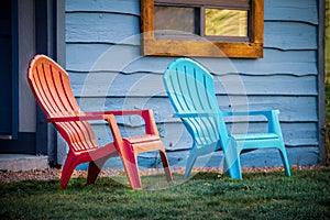 Close-up of red and turquoise arondiack chairs sitting outside blue wooden cabin door on grass