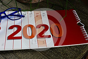 Close up of red and white isolated strip calendar on wood table for year 2020 with blue reading glasses and green plant