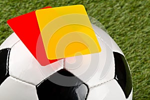 Close up of referee yellow and red cards on top of soccer ball over grass background - penalty, foul or sports concept