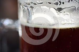 Close-Up Of Refreshing Cold Pint Of Dark Ale Beer With Condensation, Frothy Foam And Bubbles Ready To Drink