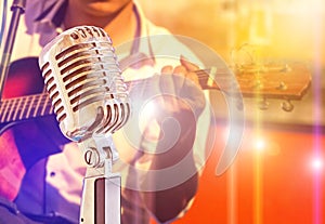 Close up retro microphone with musician playing acoustic guitar on band