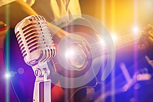 Close up retro microphone with musician playing acoustic guitar on band