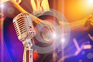 Close up retro microphone with musician playing acoustic guitar on band in night concert
