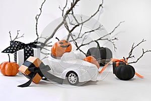 Close up retro toy car with Halloween pumpkins, gifts over tree branches. Creepy and funny decorations concept.