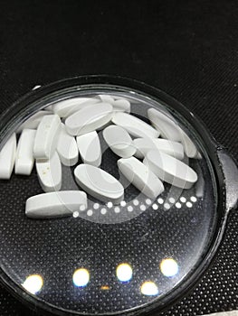 Close-up review of many white pills under the magnifying glass medicine tablets or vitamin pills in a pile Concept of healthcare,