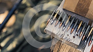 Close-up of rifle bullets on tape for machinegun stored on wooden table. Firing range. Focus on foreground. Horizontal