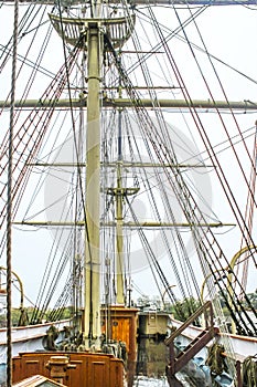 Close-up of the rigging of a wooden tall sail ship with a shiny wet wood deck against overcast sky