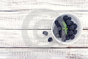 Close up of ripe blackberries in a white ceramic bowl over rustic wooden background photo