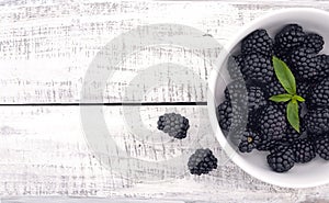 Close up of ripe blackberries in a white ceramic bowl over rustic wooden background