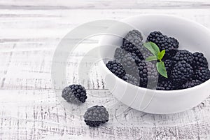 Close up of ripe blackberries in a white ceramic bowl over rustic wooden background