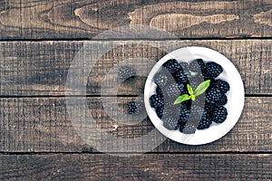 Close up of ripe blackberries in a white ceramic bowl over rustic wooden background. Top view.