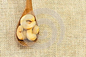 Close up roasted cashew nuts in wooden spoon on gunny sack texture