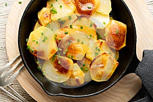 Close up Roasted potatoes slices in iron skillet with herbs. Rustic background, top view, selective focus