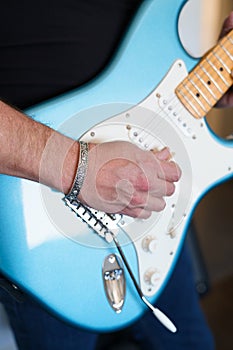 Close-up of a rock musician playing a blue electric guitar and wearing a silver cuff bracelet