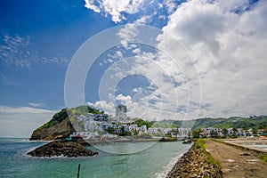 Close up of a rocky beach and buildings behind in a beautiful day in with sunny weather in a blue sky in Same, Ecuador