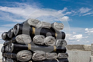 A close-up of rolls of new black roofing felt or bitumen that is precisely folded against a blue sky