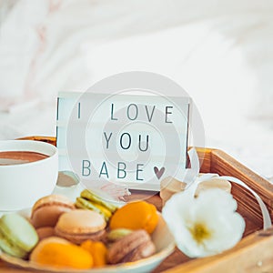 Close up Romantic Breakfast in bed with I love you baby text on lighted box. Cup of coffee, juice, macaroons, flower and gift box