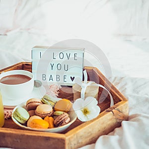 Close up Romantic Breakfast in bed with I love you baby text on lighted box. Cup of coffee, juice, macaroons, flower and gift box