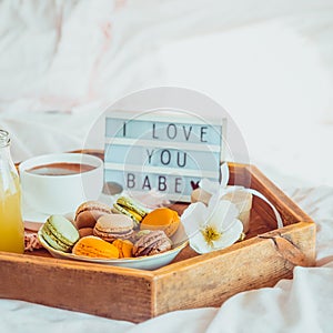 Close up Romantic Breakfast in bed with I love you baby text on lighted box. Cup of coffee, juice, macaroons, flower and gift box