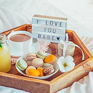 Close up Romantic Breakfast in bed with I love you baby text on lighted box. Cup of coffee, juice, macaroons, flower and gift box