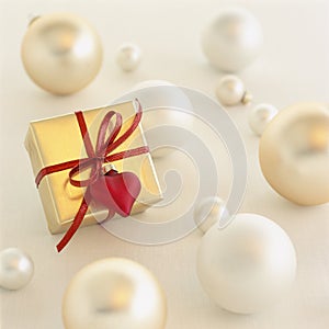 Close-up of romantic Christmas gift present with gold wrapping paper and red heart decoration surrounded by Christmas ornaments on