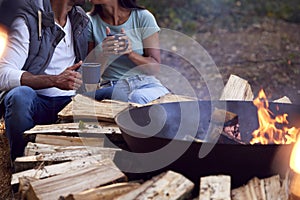 Close Up Of Romantic Couple Camping Sitting By Bonfire In Fire Bowl With Hot Drinks