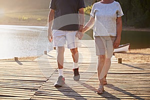 Close Up Of Romantic Senior Couple Walking On Jetty By Lake