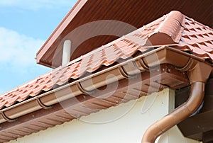 Close up on roof gutter holder and guttering downspout pipe with clay tiles roof. Installing rain gutter.