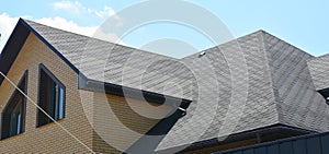 A close-up on a roof problem area covered with asphalt roof shingles and irregular shape window on the wall of the house