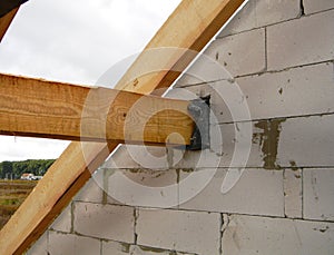 A close-up on a roofing frame construction, attaching, anchoring roof beams, trusses and braces to the brick wall of the house