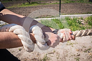 Close-up rope in hands of man, play tug of war in outdoors