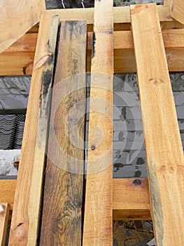 A close-up on rotten, damaged with mold and mildew wood, boards, timber and new untreated timber boards, planks on a brick house