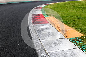 Close up of rough curb at right turn motor sport track with green field and black asphalt