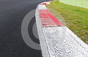 Close up of rough curb at right turn on motorsport track with green field and black asphalt