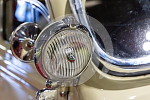 Close-up of the round headlamps of a beige classic car.