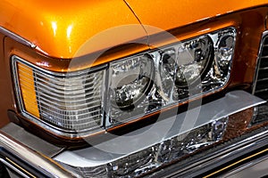 Close-up of the round headlamps of a orange american classic car.