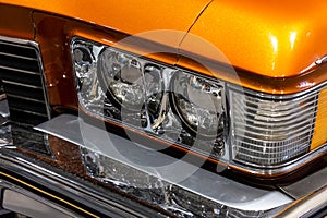 Close-up of the round headlamps of a orange american classic car.