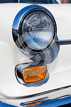 Close-up of the round headlamps and orange turn signal of a white classic car.