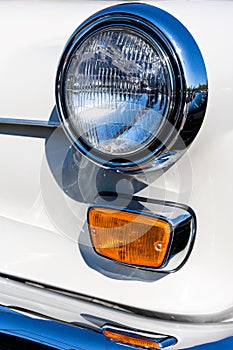 Close-up of the round headlamps and orange turn signal of a white classic car.