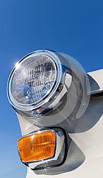 Close-up of the round headlamps and orange turn signal of a white classic car.