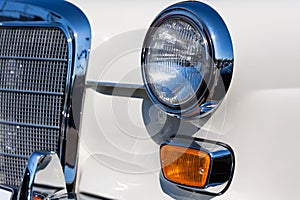 Close-up of the round headlamps and orange turn signal of a white classic car.