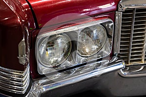 Close-up of the round headlamps of a red american classic car.