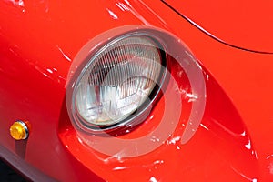 Close-up of the round headlamps of a red, sport classic car.