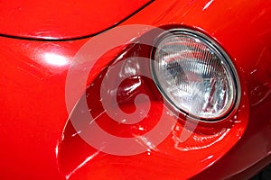 Close-up of the round headlamps of a red, sport classic car.
