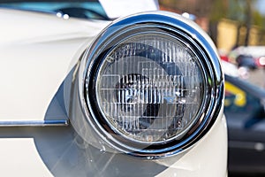Close-up of the round headlamps of a white classic car.